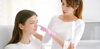Dermatolog w rękawiczkach bada policzek pacjentki trzymającej lusterko.